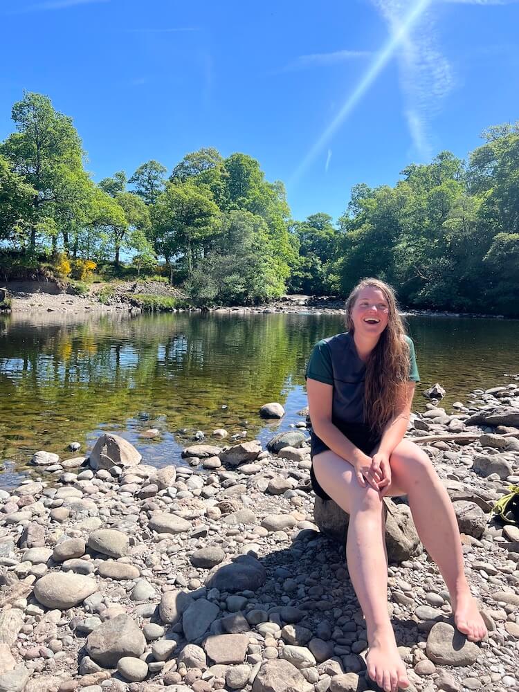 girl sitting by river in Perthshire laughing