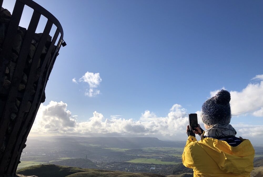 Girl on top of Dumyat hill overlooking Stirling and surrounding landscape takiing photo