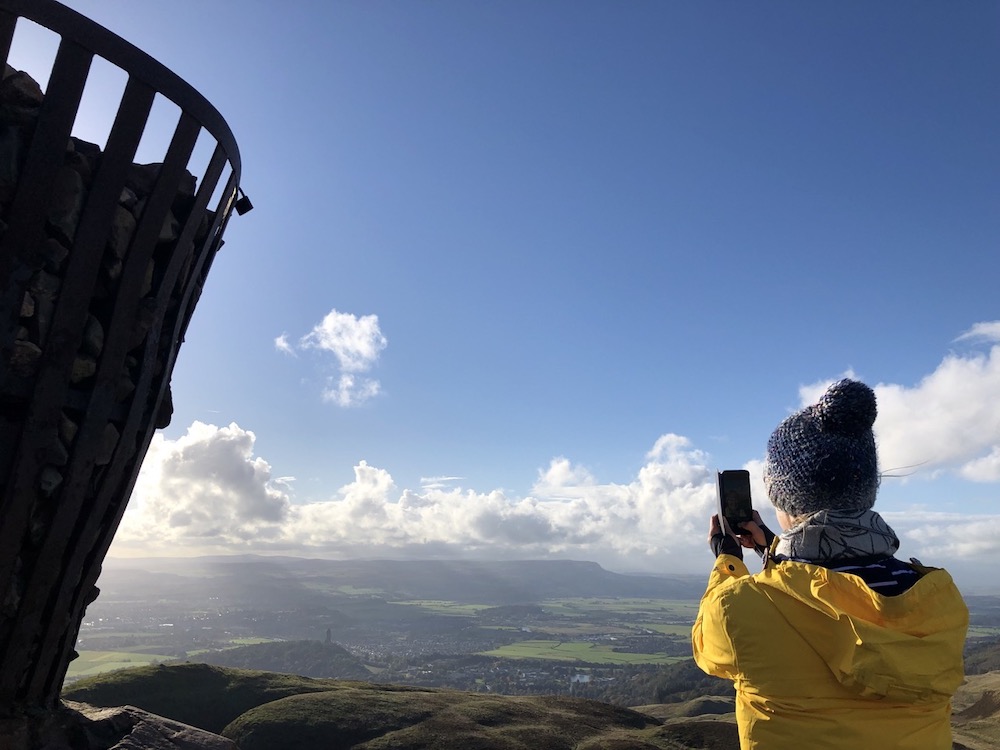 Girl on top of Dumyat hill overlooking Stirling and surrounding landscape takiing photo