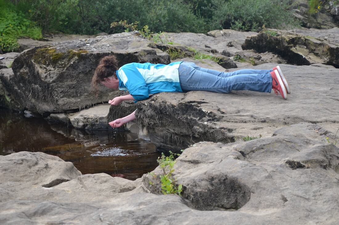 Ruth Pringle lying on rocks and investigating a small pool of water during a Blue Noun activity in Scotland.